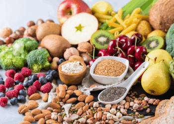A variety of high-fiber foods including chia seeds, berries, whole wheat pasta, vegetables, and oats arranged on a rustic table