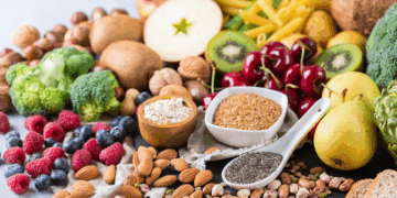 A variety of high-fiber foods including chia seeds, berries, whole wheat pasta, vegetables, and oats arranged on a rustic table